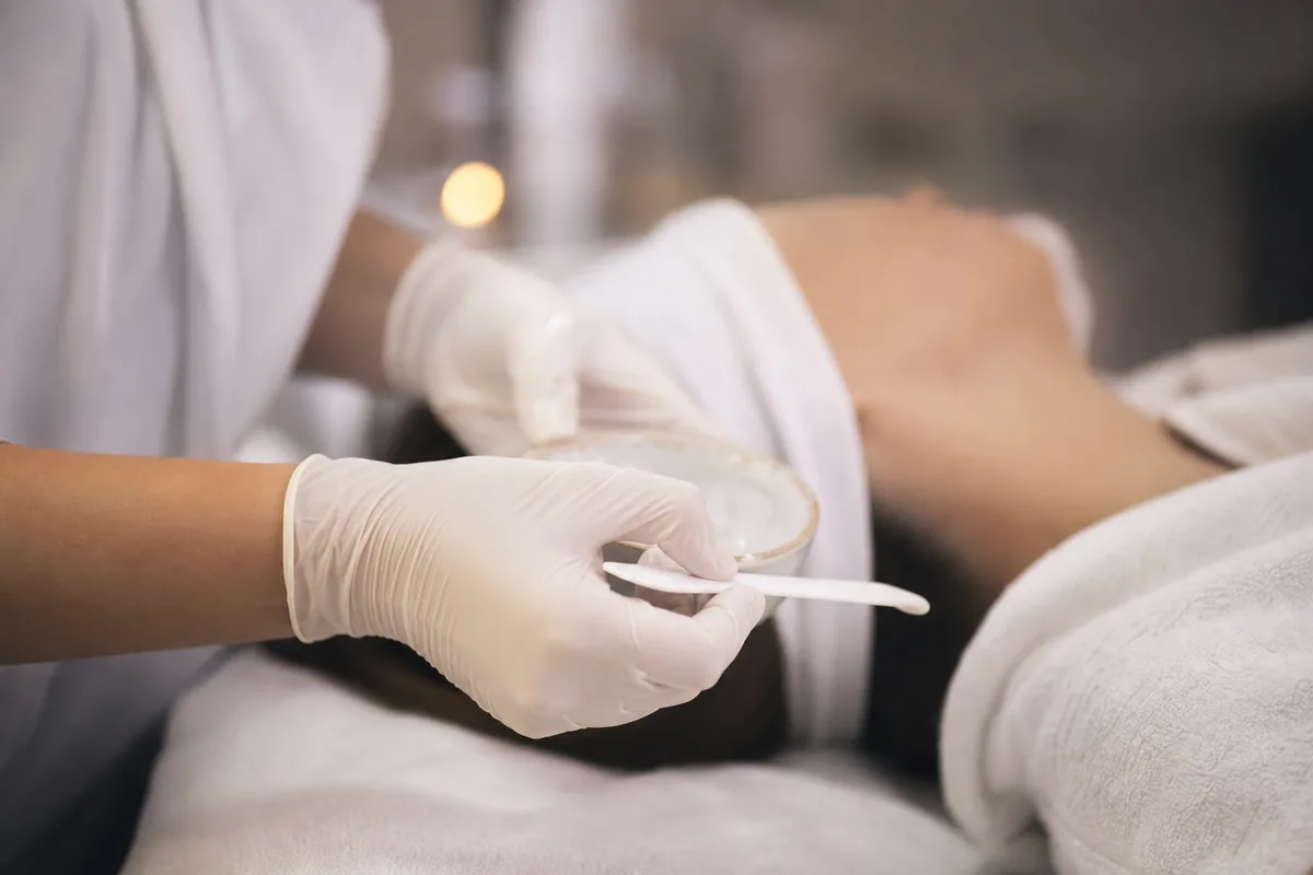Gros plan sur les mains d’une praticienne réalisant un soin du visage en institut, sans visage visible